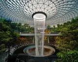 Wodospad HSBC Rain Vortex w porcie lotniczym Singapur-Changi, otoczony bujną zielenią i przejeżdżającymi pociągami.