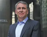 Ken Griffin, w eleganckim garniturze, stoi przed budynkiem z napisem "CITADEL".