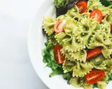 Pyszny makaron z pesto, udekorowany pomidorkami koktajlowymi i świeżą sałatą, podany na białym talerzu.