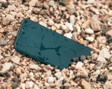 Smartfon leży na kamieniach, mokry, ale wytrzymały zgodnie ze **standardem militarnym MIL-STD-810H**.