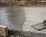 Świeżo wylany beton na budowie, z widoczną kielnią i drewnianym klockiem. Czas schnięcia cementu w ziemi zależy od wielu czynników.