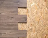 Deska drewnopodobna na tle płyty OSB. Wymiary płyty OSB są widoczne w odsłoniętych fragmentach.