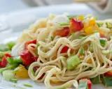 Ein bunter asia nudelsalat mit Paprika und Frühlingszwiebeln auf einem weißen Teller.