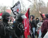 Demonstranten mit Fahnen, darunter eine mit der Aufschrift "System Metternich", und Polizisten in Schutzkleidung.