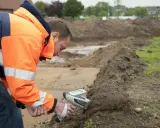 Pracownik w pomarańczowej kurtce wykonuje badanie gruntu za pomocą specjalistycznego urządzenia.