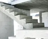 Surowe, betonowe schody czekają na wykończenie. W tle białe bloczki budowlane.