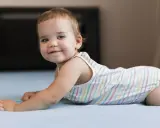 Un adorabile neonato di 8 mesi, con occhi azzurri e un sorriso contagioso, gioca sul letto.