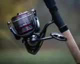 Czarne, nowoczesne detale budowy kołowrotka wędkarskiego Daiwa Ninja LT 4000-C z szarą żyłką i korkową rękojeścią.