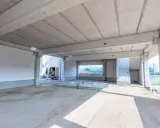 Betonowy strop teriva w stanie surowym, z widocznymi belkami i płytami. W tle samochód dostawczy i schody.