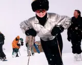 Ivana Trump joven, sonriendo y esquiando con un gorro de piel y gafas de esquí. A su alrededor, otras personas disfrutan de la nieve.
