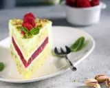 Pyszny tort pistacjowo malinowy z malinami i miętą na talerzu. Obok widoczne łuskane pistacje.