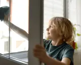 Chłopiec z uśmiechem na twarzy wykonuje jedno z domowych obowiązków – myje okno.