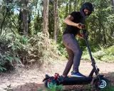 Un homme en casque roule en trottinette électrique dans une forêt. Il semble rencontrer un problème, peut-être un code erreur e8 trottinette électrique.