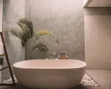 Relajante bañera exenta rodeada de piedras blancas, toallas dobladas en una escalera de madera y una planta tropical. Un ejemplo de cuartos de baño modernos y serenos.