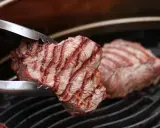 Zangen halten ein saftiges Stück Roastbeef, das auf einem Grill zubereitet wird.