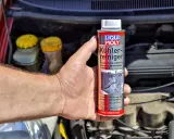 Dłoń trzyma puszkę preparatu Liqui Moly do płukania układu chłodzenia. W tle widać silnik samochodu.