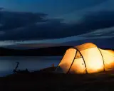 Upplyst tält vid en sjö i skymningen. En cykel står parkerad bredvid. Perfekt för camping Sverige karta-äventyr.