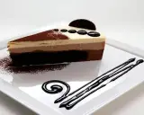 Una rebanada de tarta de tres chocolates, con capas de mousse de chocolate blanco, con leche y negro, espolvoreada con cacao y decorada con chocolate.