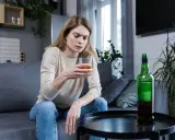 Kobieta z kieliszkiem alkoholu i butelką obok. Obraz symbolizuje 10 strat z picia alkoholu, pokazując jej smutek i zagubienie.