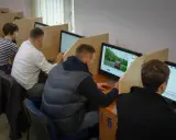 Ludzie siedzą przy komputerach, rozwiązując testy. Zastanawiają się, ile trzeba mieć punktów, żeby zdać teorię na prawo jazdy.