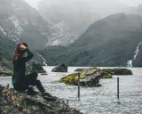 Kobieta w kapeluszu podziwia surowe piękno norweskiej przyrody. Woda, góry i wodospad tworzą malowniczy krajobraz, który oddaje esencję życia w Norwegii.