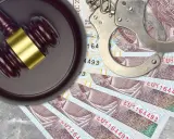 Młotek sędziowski, kajdanki i polskie banknoty na szarym tle.