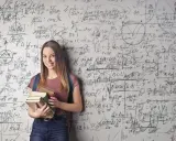 Uśmiechnięta studentka z książkami przed ścianą pełną równań matematycznych. Zastanawia się, co po studiach matematycznych.