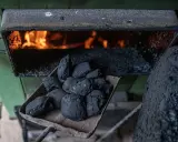 Łopata z węglem brunatnym czeka na załadunek do pieca węglowego. W palenisku żarzą się płomienie, gotowe do ogrzania domu.