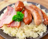 Assiette de choucroute allemande ou alsacienne garnie de saucisses et de lardons, décorée d'une touche de persil frais.