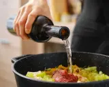 Una mano vierte vino en una sartén con ingredientes. El vino en moderación realza el sabor de la comida.
