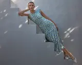 A woman in a floral dress and white heels, embodying a chic formal dress code for women, poses on white stairs.