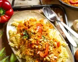 Fusilli mit einer herzhaften bolognese mit roten linsen, garniert mit Erdnüssen und Petersilie. Daneben liegen eine rote Paprika und Knoblauch.