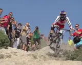 Kolarz w akcji podczas zawodów MTB, otoczony przez kibiców i fotografów.