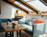 Przytulne poddasze w drewnie, skosy dachowe i okna połaciowe tworzą ciepłą atmosferę. Jasny salon z sofą i fotelem.