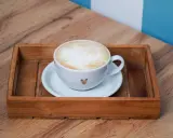 Eine Tasse Kaffee au lait mit Herz-Detail auf einem Holzteller, bereit zum Genießen.