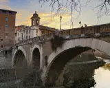El puente Fabricio, con sus arcos de piedra y la torre medieval, cruza el Tíber bajo un cielo anaranjado.