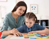 Terapeuta pomaga dziecku z niepełnosprawnością intelektualną układać kolorowe puzzle.