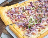 Flammkuchen varianten: knuspriger Teig mit Speck, Zwiebeln und Schnittlauch belegt.