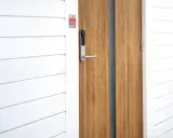 En modern ytterdörr med ett Verisure Yale Doorman V2N lås. Dörren är i trä och har en vitmålad panelvägg bredvid.
