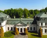 Pałac w Sieniawie, z zielonym dachem i jasną fasadą, otoczony jest bujną zielenią.