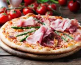 Pyszna pizza ze szparagami i szynką parmeńską, ozdobiona świeżymi pomidorkami koktajlowymi.
