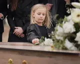 Smutne dziecko na pogrzebie, dotyka kwiatów na trumnie. W tle dorośli w czerni. Czy to dziecko wierzy w przesądy?