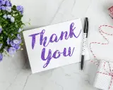 Carte "Thank You" violette, entourée de fleurs bleues, d'un stylo étoilé et d'un cadeau emballé. Une belle façon de remercier quelqu'un pour sa gentillesse.