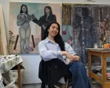 A young woman, one of many talented gen z artists, smiles in her studio, surrounded by her evocative paintings.