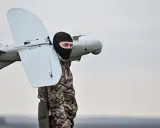 Mann in Tarnkleidung und schwarzer Sturmhaube trägt eine Drohne. Seit wann gibt es Drohnen? Die Geschichte reicht weit zurück.