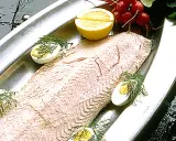 En vacker inkokt lax serveras på ett silverfat med citronklyftor, kokta ägg och dill.