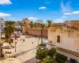 Tunezja Sousse czy warto? Rynek z palmami, zabytkową wieżą i flagami. Słoneczny dzień zachęca do zwiedzania.