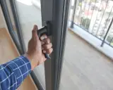 Dłoń chwyta za klamkę, wykonując regulację drzwi balkonowych dwuskrzydłowych. Widok na balkon i miasto.
