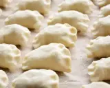 Gotowe do gotowania ciasto na pierogi, ułożone rzędami na blacie.