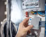 Dłoń montuje bezpiecznik w rozdzielnicy, kluczowy element domowej instalacji elektrycznej.